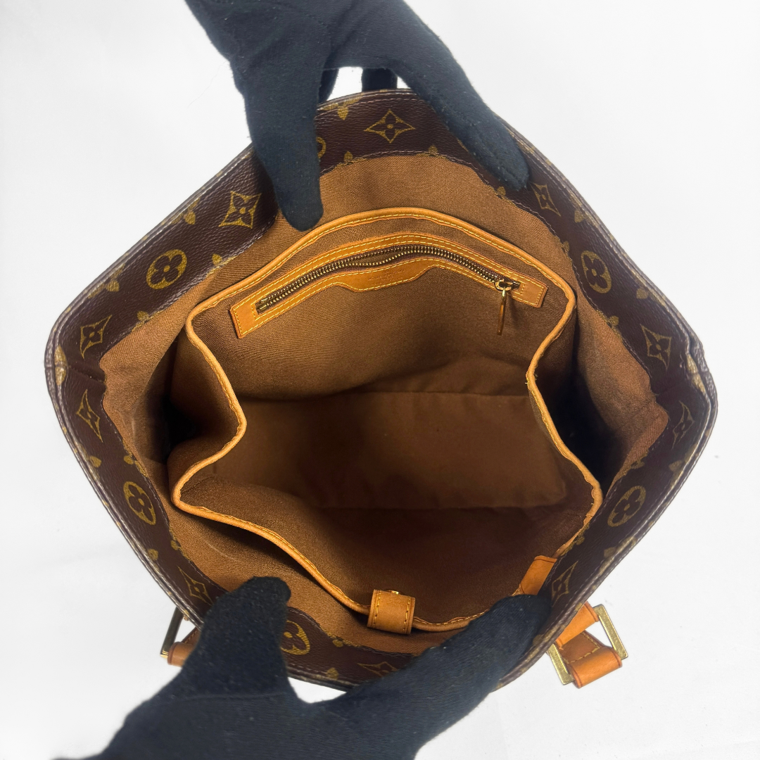The interior of a Louis Vuitton monogram bag, shown from above, held open by two hands wearing black gloves against a white background.