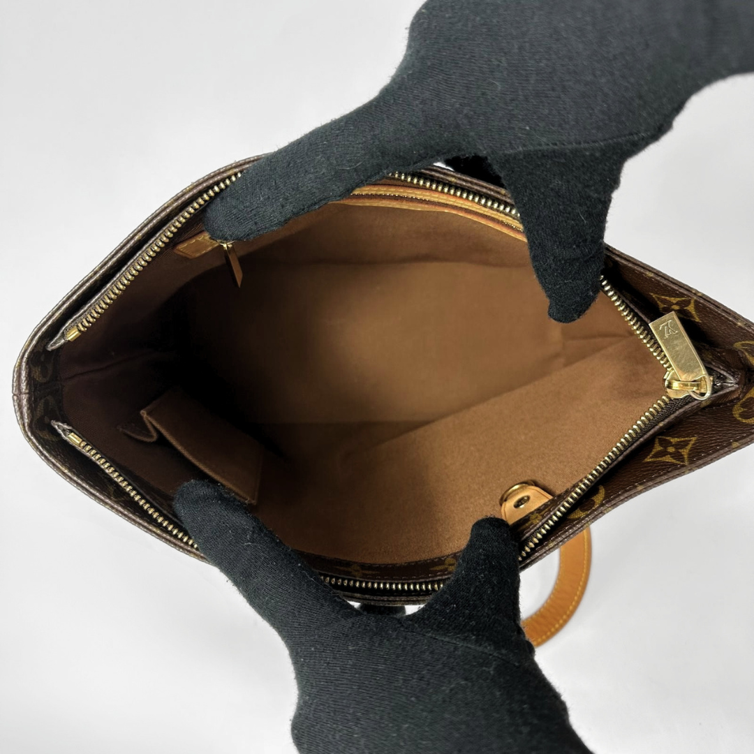 Louis Vuitton monogram canvas handbag shown open from above, with black gloves holding the zipper area against a plain light background.