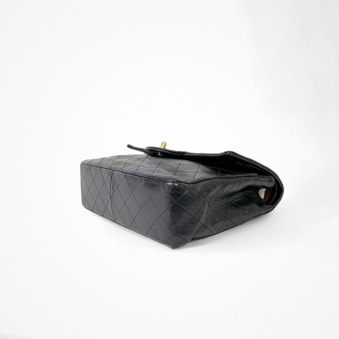 Black Chanel handbag with gold chain and clasp on a white background