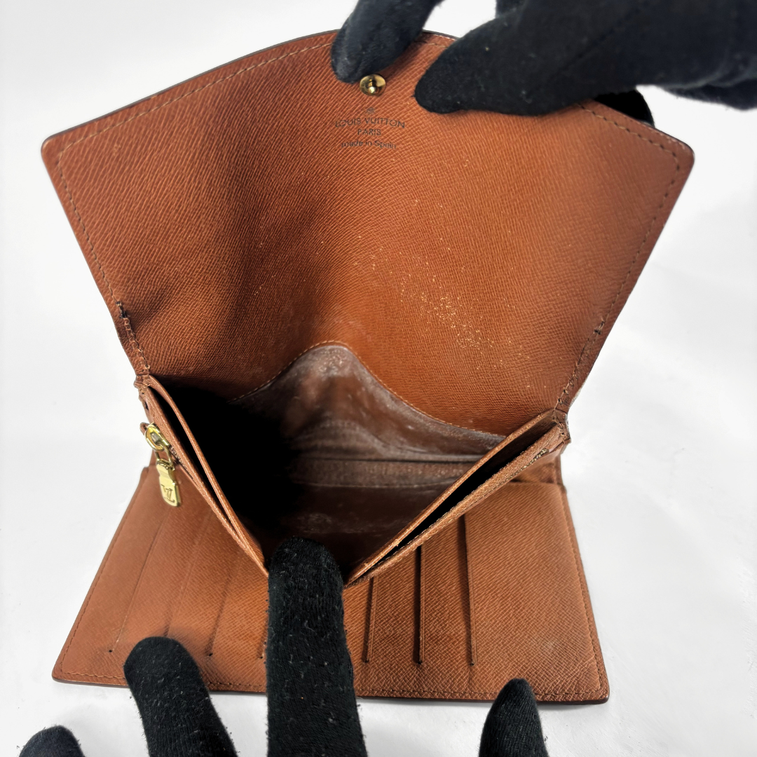 A brown textured leather wallet opened wide by black-gloved hands, showing its interior compartments and gold-tone hardware against a plain white background.