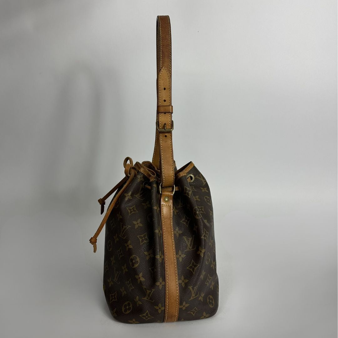 A Louis Vuitton monogram canvas bucket bag with tan leather trim and a drawstring closure, photographed against a neutral light gray background.