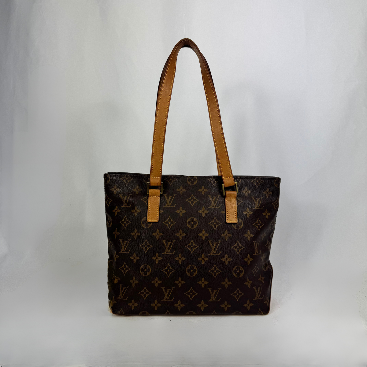 A Louis Vuitton monogram canvas tote bag with tan leather shoulder straps, photographed against a plain light gray studio background.