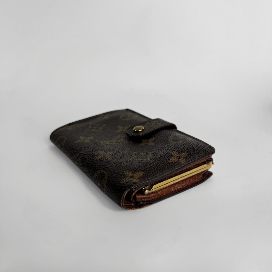 A Louis Vuitton monogram bifold wallet in dark brown coated canvas with gold-tone hardware, photographed on a light gray studio background.