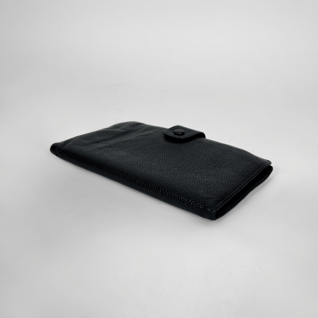 A black textured leather wallet with a snap-button closure, photographed on a light gray studio background.