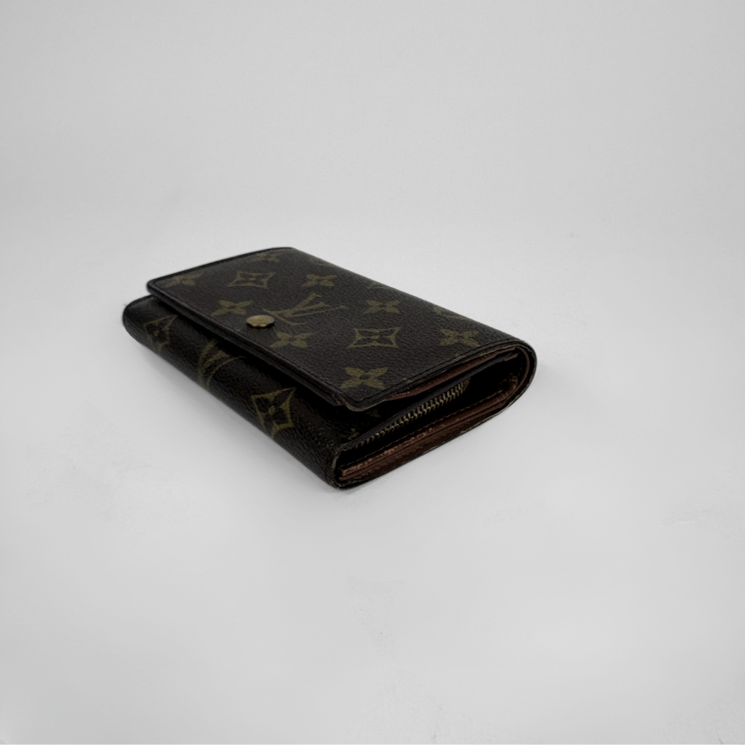 A dark brown Louis Vuitton monogram canvas bi-fold wallet with a gold-tone snap button and zipper, photographed on a light gray background.