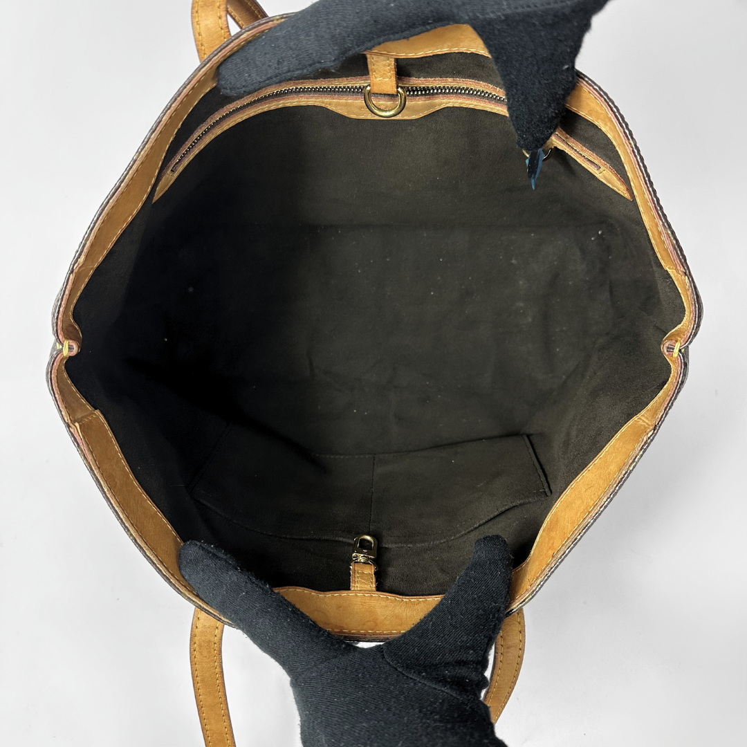 An open black leather shoulder bag with tan leather trim, shown from a top-down view against a light gray background.