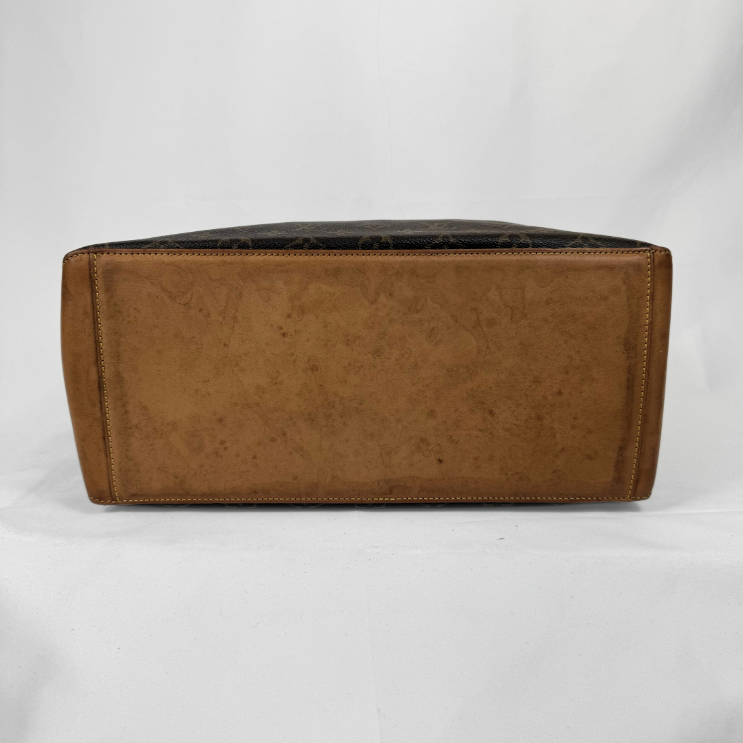 A Louis Vuitton monogram canvas tote bag shown from the bottom, featuring a brown coated canvas body with the classic dark brown monogram pattern and tan leather trim, photographed against a white studio background.