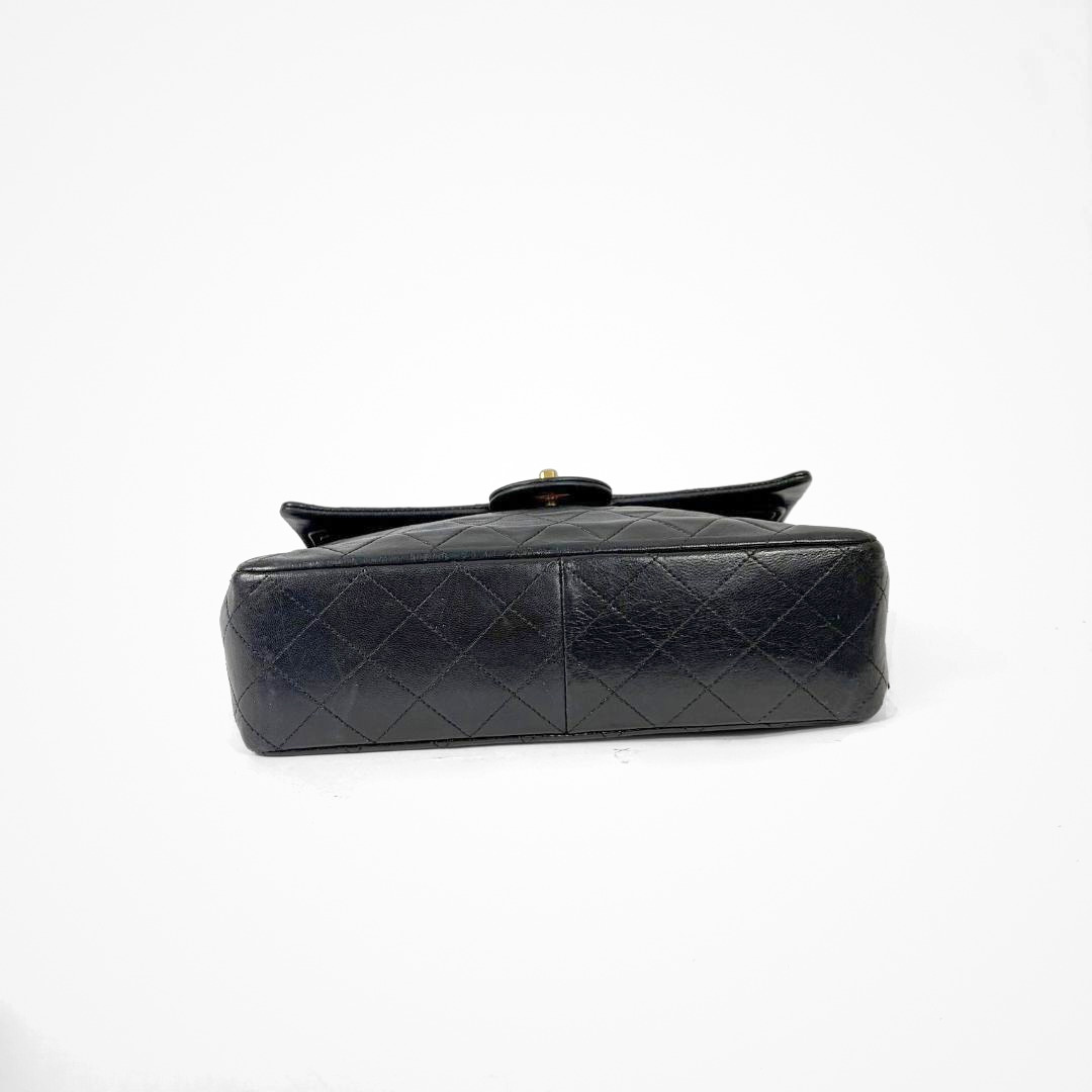 Black Chanel handbag with gold chain and clasp on a white background