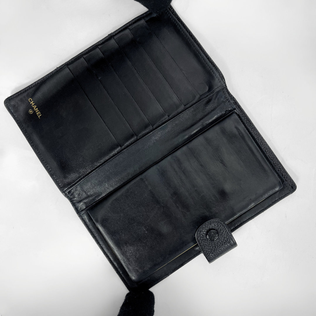 An open black leather wallet with multiple card slots and a large slip pocket, featuring a small gold CHANEL logo on the left side, photographed on a white background.