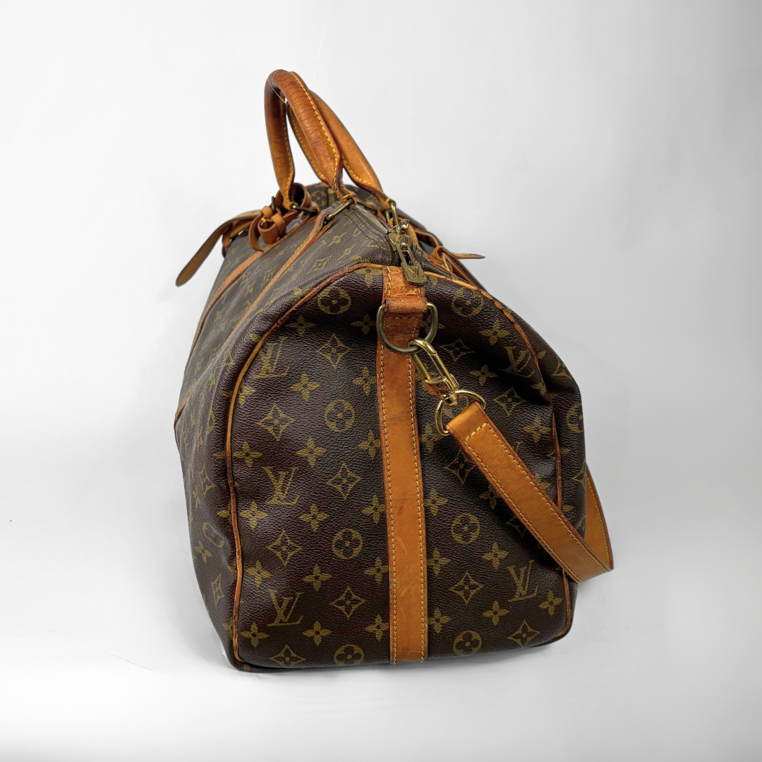 Brown monogram patterned travel bag with tan leather handles and strap on a white background