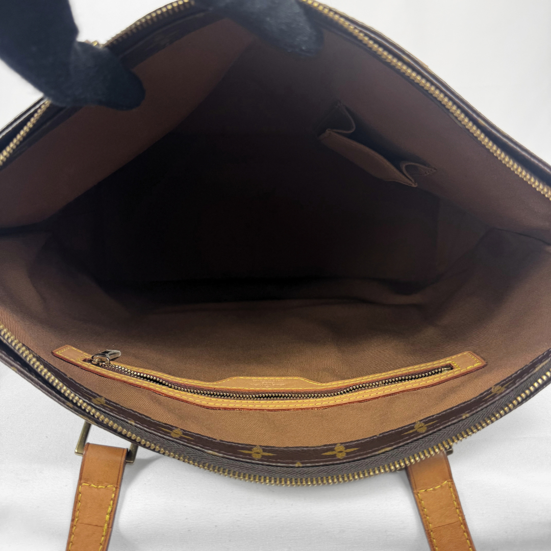 Open view of a Louis Vuitton monogram handbag showing the brown interior lining, gold-tone zipper, and tan leather strap against a white background.