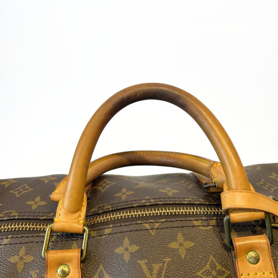 Close-up of a brown leather handle on a Louis Vuitton monogram bag.