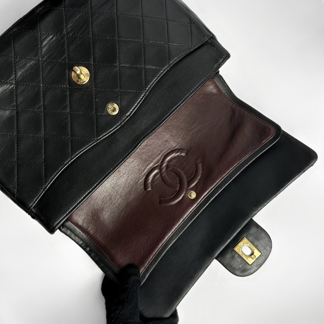 Black quilted handbag with brown leather flap and gold hardware on a white background