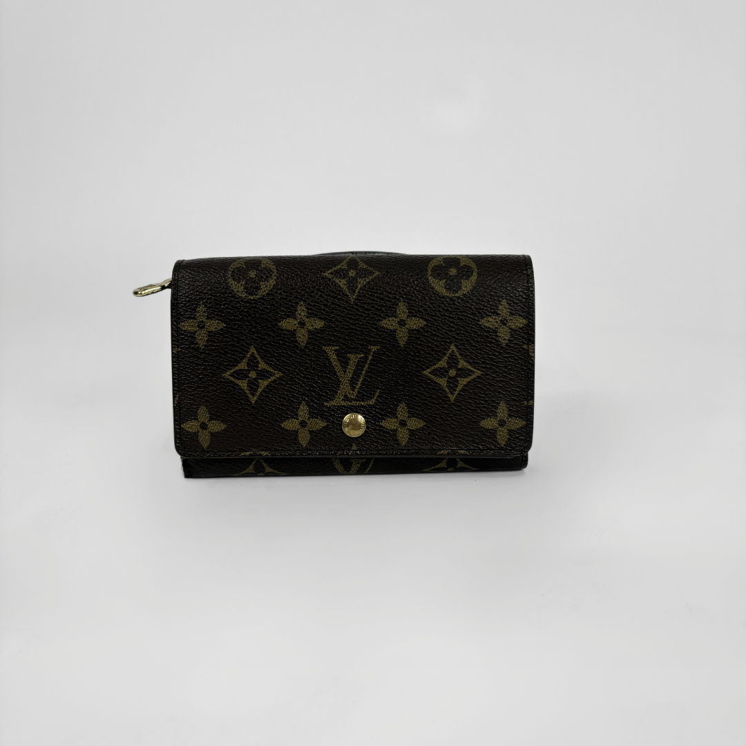 A Louis Vuitton monogram canvas wallet in black with gold-tone hardware, photographed against a plain light gray background.