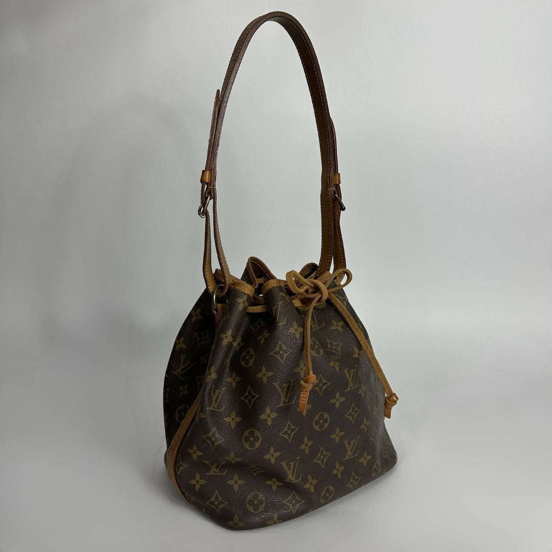 A Louis Vuitton monogram canvas bucket bag with a brown leather shoulder strap and drawstring closure, photographed against a neutral light gray background.