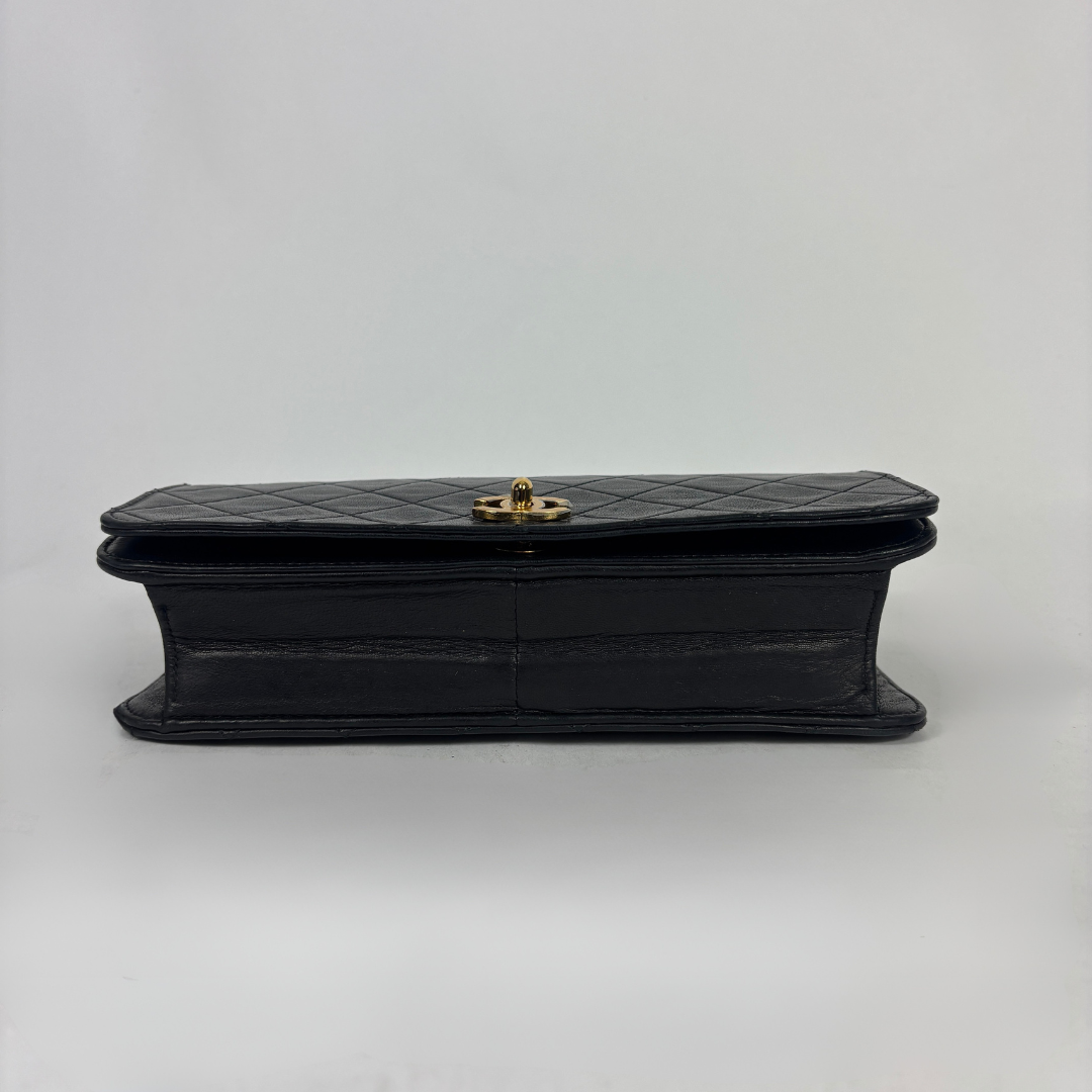 A black quilted leather clutch bag with a gold-tone turn-lock clasp, shown from the side against a plain light gray background.