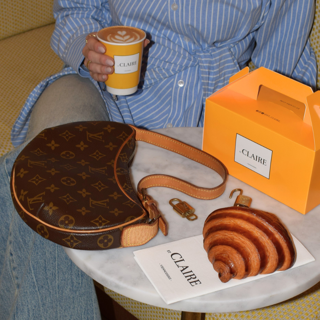 Person holding a coffee cup with a 'Claire' branded box and pastry on a table.